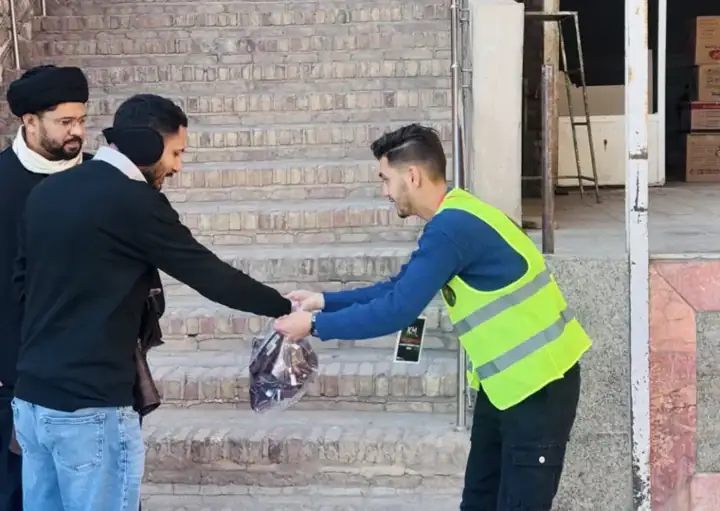 KBM volunteer handing a bag to a pilgrim on the steps of a shrine